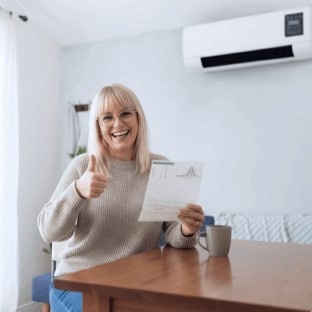 Happy woman giving thumbs up with EpiCooler wall air conditioner mounted in living room – satisfied customer